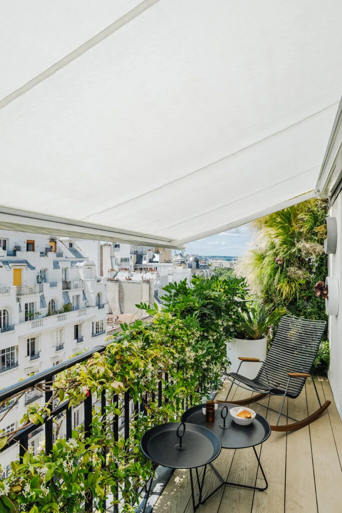 Balcon parisien avec store banne, transat design et végétation luxuriante offrant une vue dégagée sur les toits