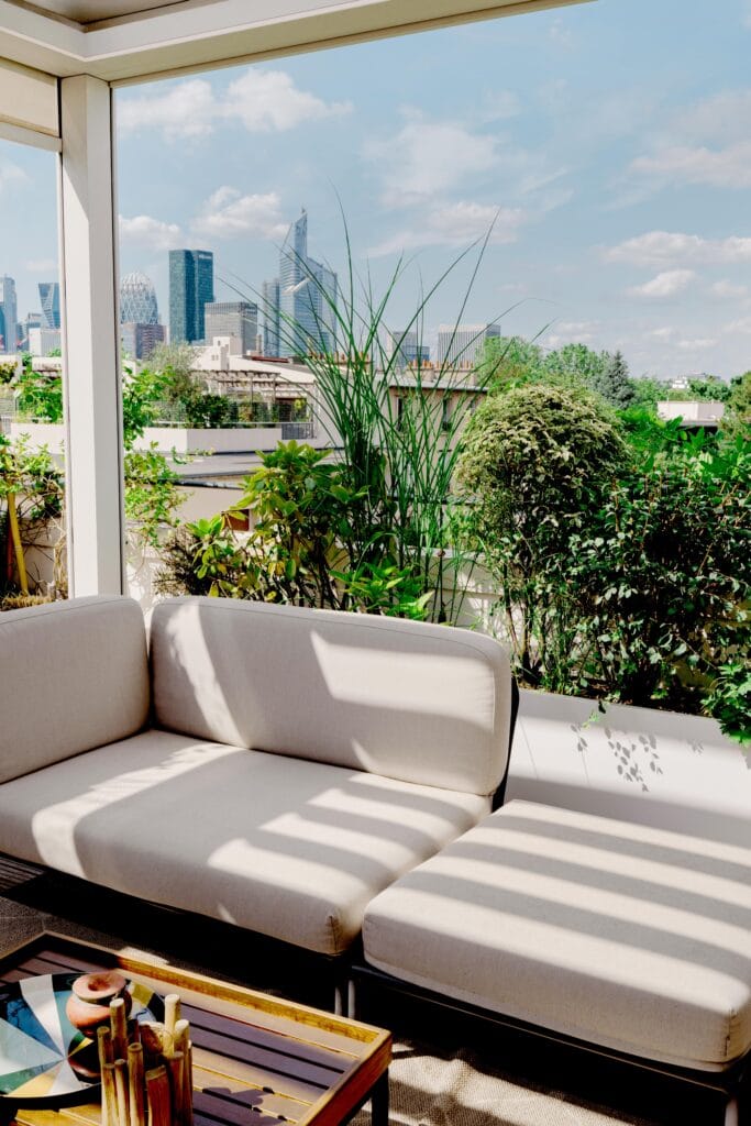 Salon de terrasse avec canapé clair et jardinières blanches face aux tours de La Défense