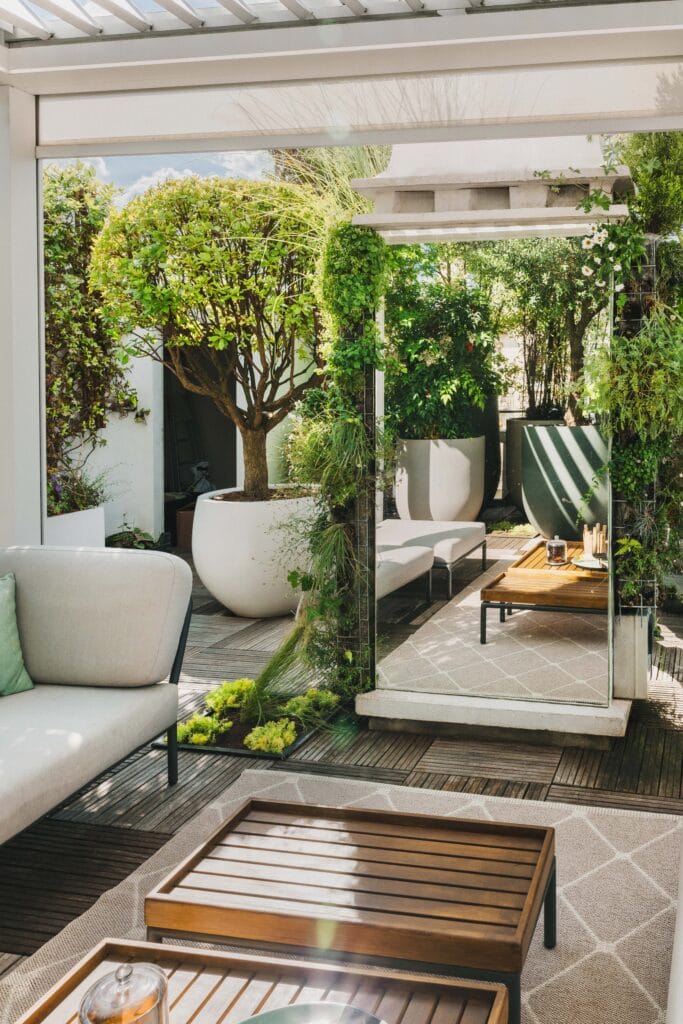 Miroir de jardin habillé de plantes grimpantes reflétant une terrasse aménagée en bois.