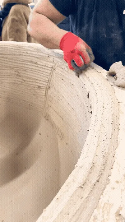 Main gantée rouge appliquant une texture ou un enduit sur le bord d'un grand pot de jardin en terre cuite, illustrant le savoir-faire artisanal