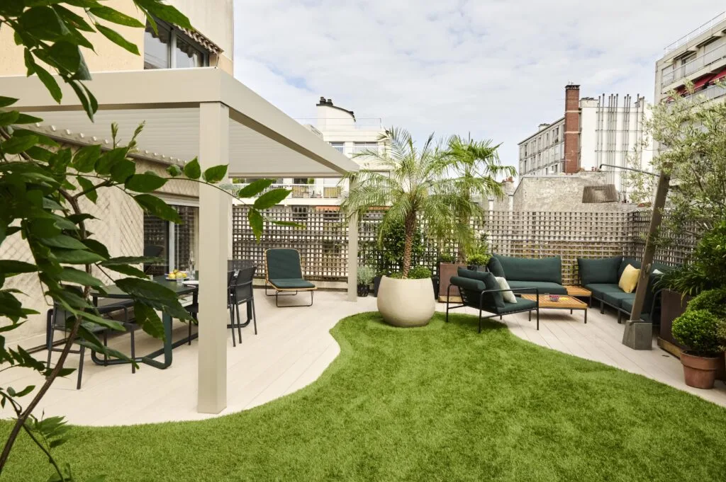Grande terrasse de toit avec coin repas, salon de jardin vert et îlot de gazon artificiel entouré de grands pots de fleurs