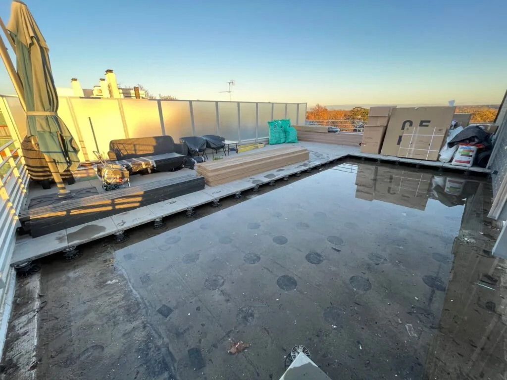 Terrasse avant aménagement montrant un sol dégradé avec stagnation d’eau et matériel de chantier