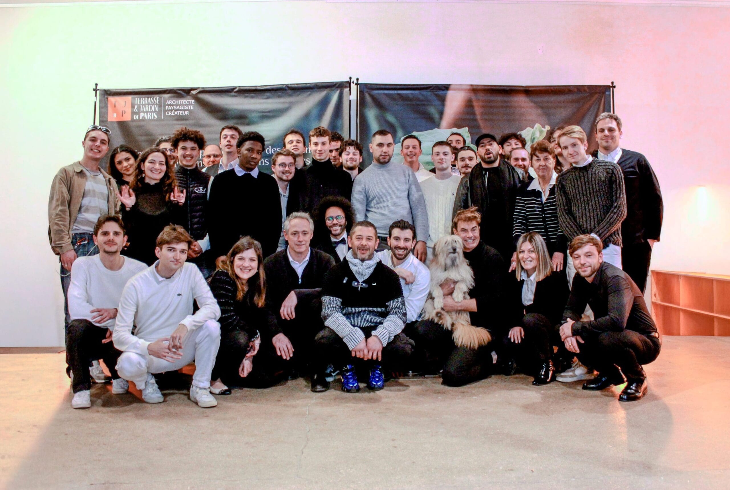 Portrait de groupe de l'équipe Terrasse et Jardin de Paris réunie devant un visuel de la Maison. Architectes, paysagistes et artisans posent ensemble en intérieur.