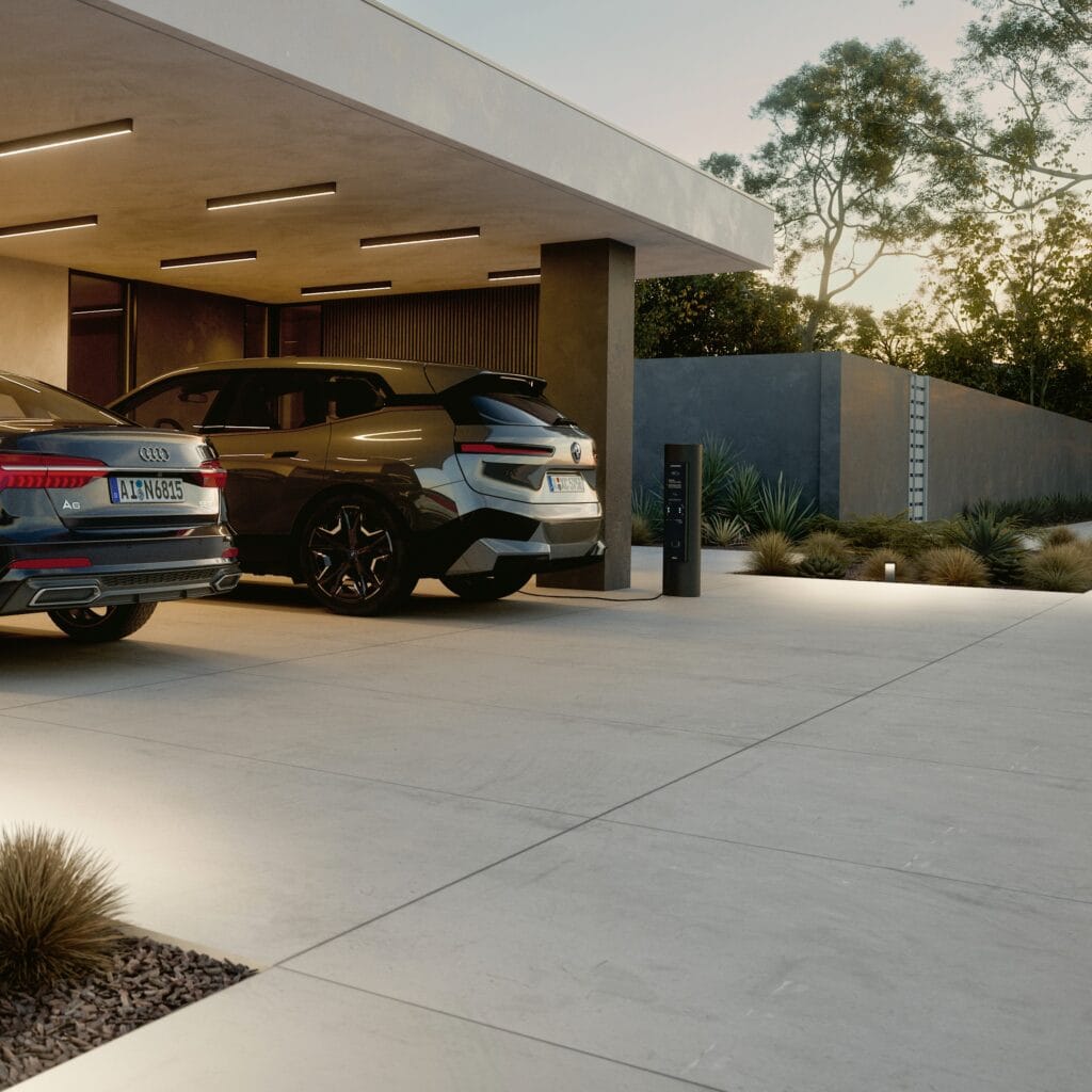 Borne de recharge Bega intégrée dans allée de villa contemporaine avec carport, véhicules électriques premium et aménagement paysager