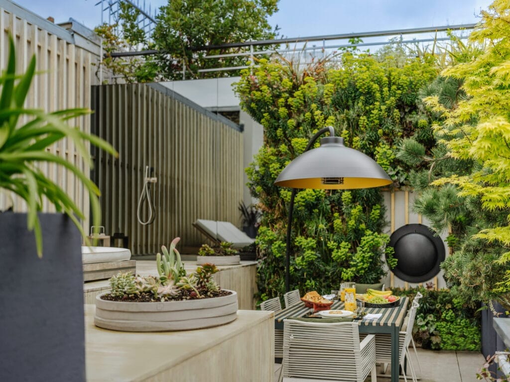 Terrasse paysagère aménagée par TJDP avec mur végétal, lampe chauffante design, mobilier extérieur et jardinières de succulentes à Paris